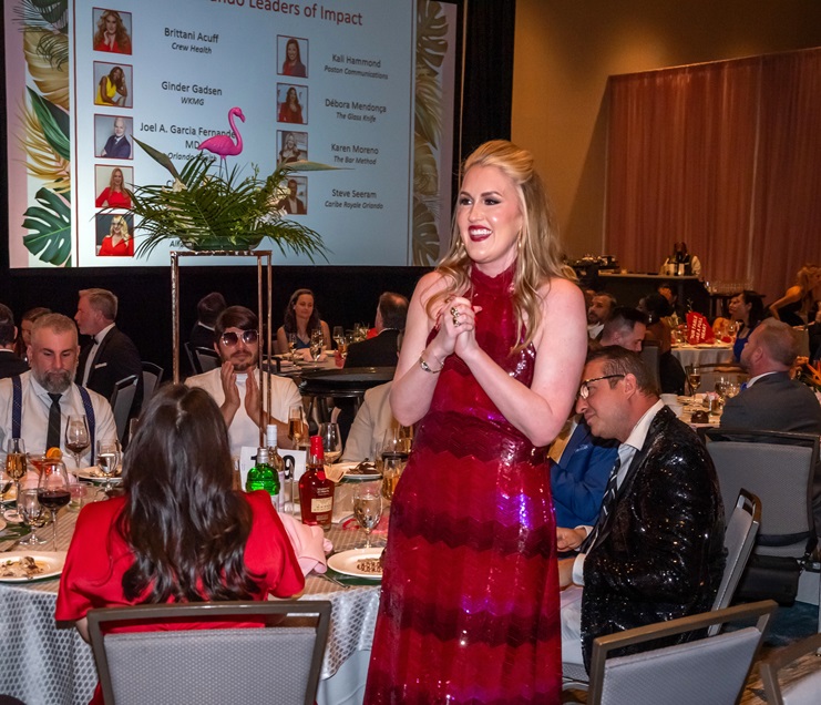 Woman in red standing by table while audience applauds
