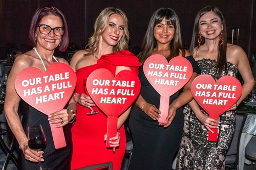 Four women holding up heart shaped signs reading Our table has a full heart