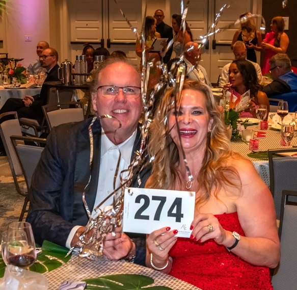 Couple surrounded by streamers holding up bidder paddle 274